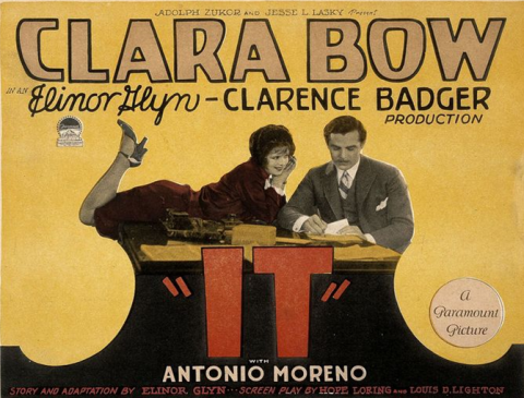 Woman laying on her stomach and man standing over the word It