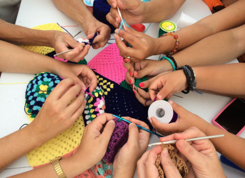 A group of hands crocheting various projects. 
